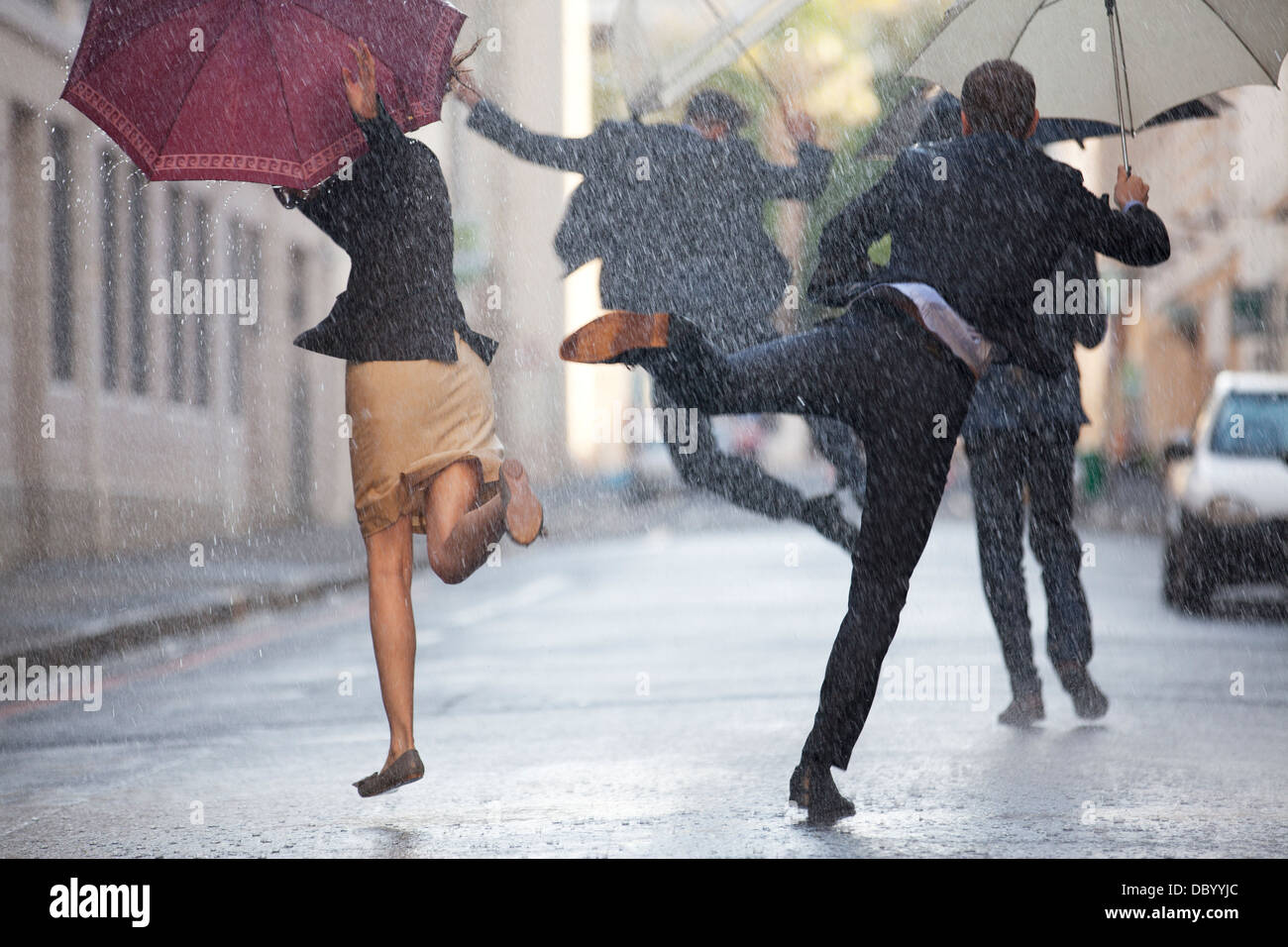 La gente di affari con ombrelloni dancing in Rain Foto Stock