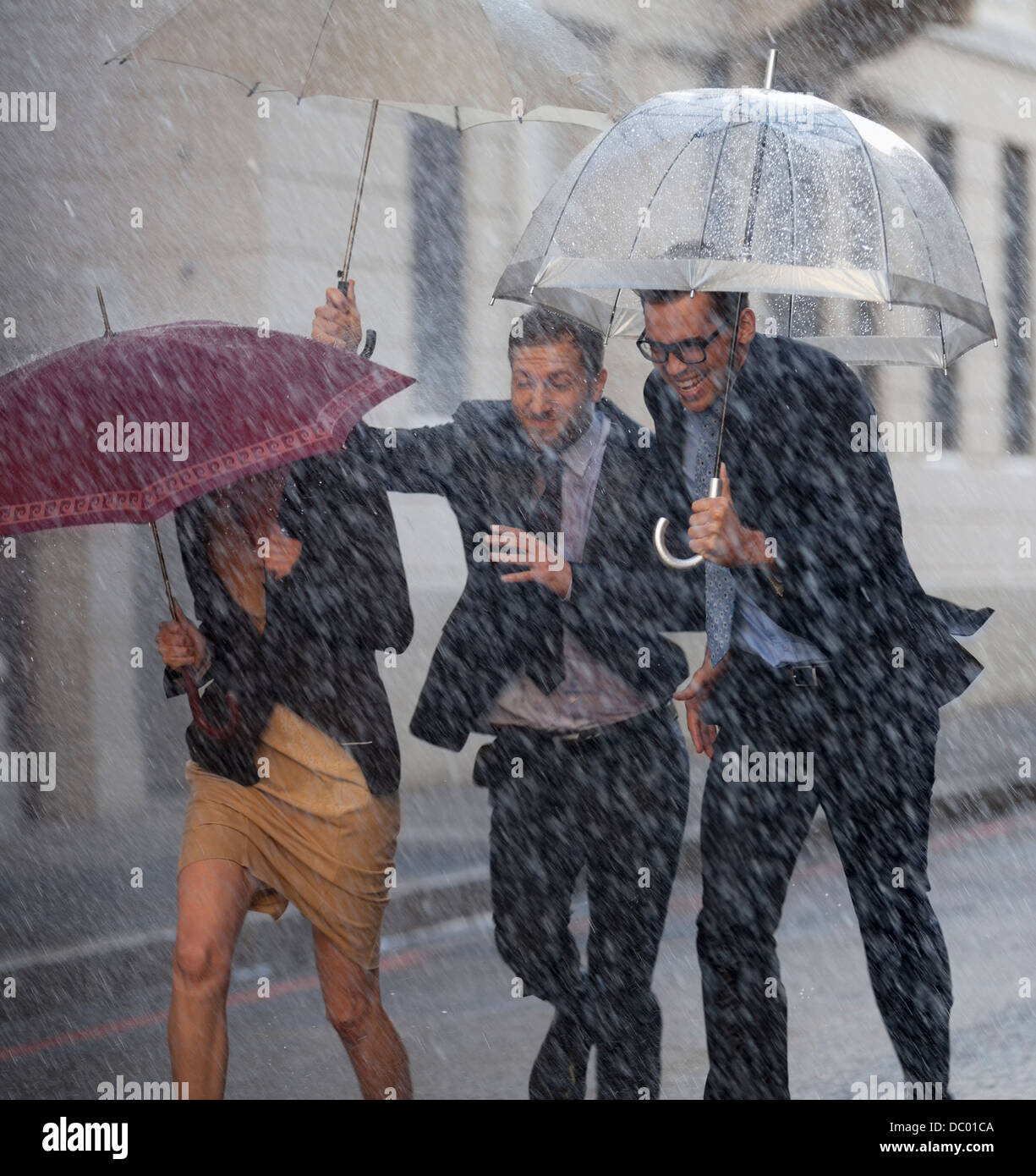 Felice la gente di affari con ombrelloni in esecuzione in rainy street Foto Stock