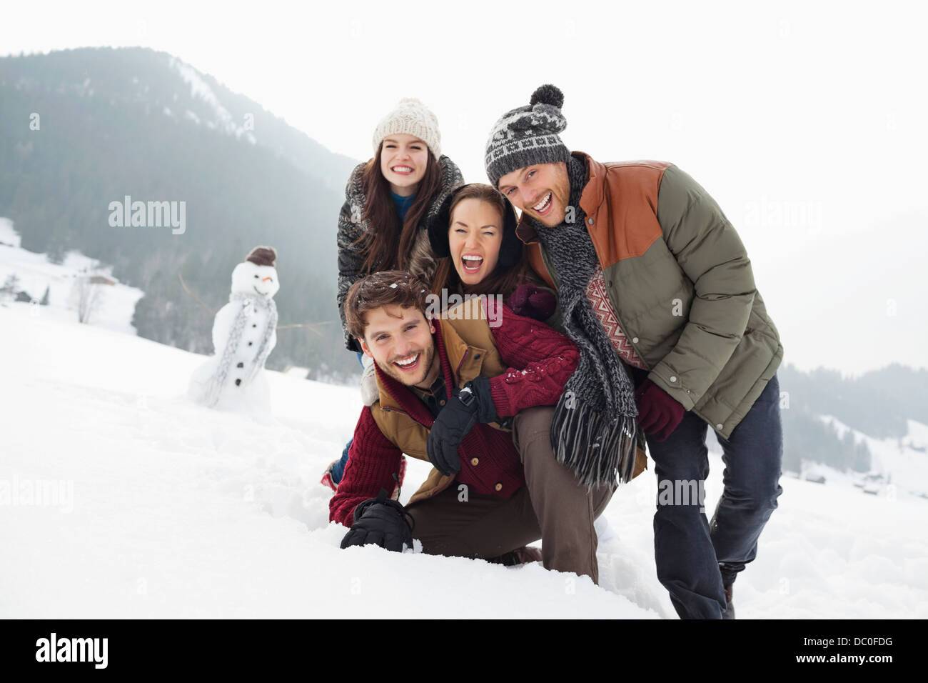 Ritratto di felice amici in campo nevoso con pupazzo di neve Foto Stock