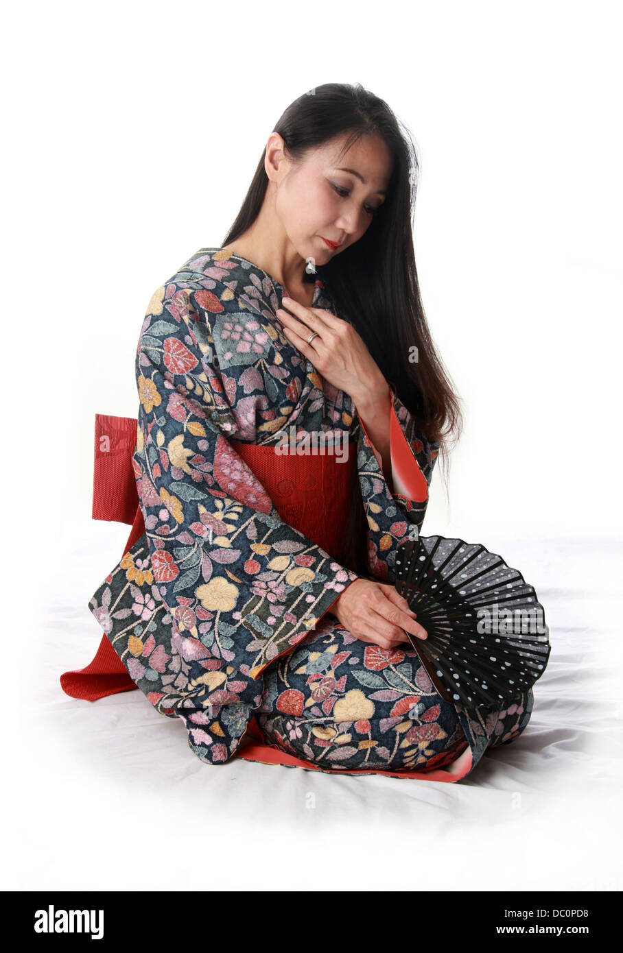 Giapponese signora seduta sul pavimento indossando un tradizionale di blu e di rosso modellato kimono e tenendo una ventola Foto Stock