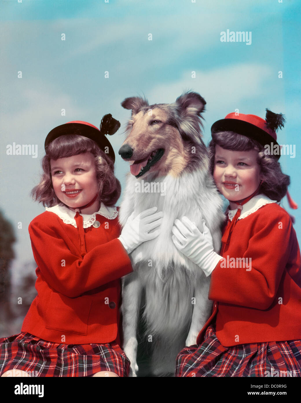 1940s ritratto sorridente TWIN ragazze indossano MATCHING MAGLIONI ROSSO PLAID GONNE Cappelli e guanti in posa con cane Collie Foto Stock