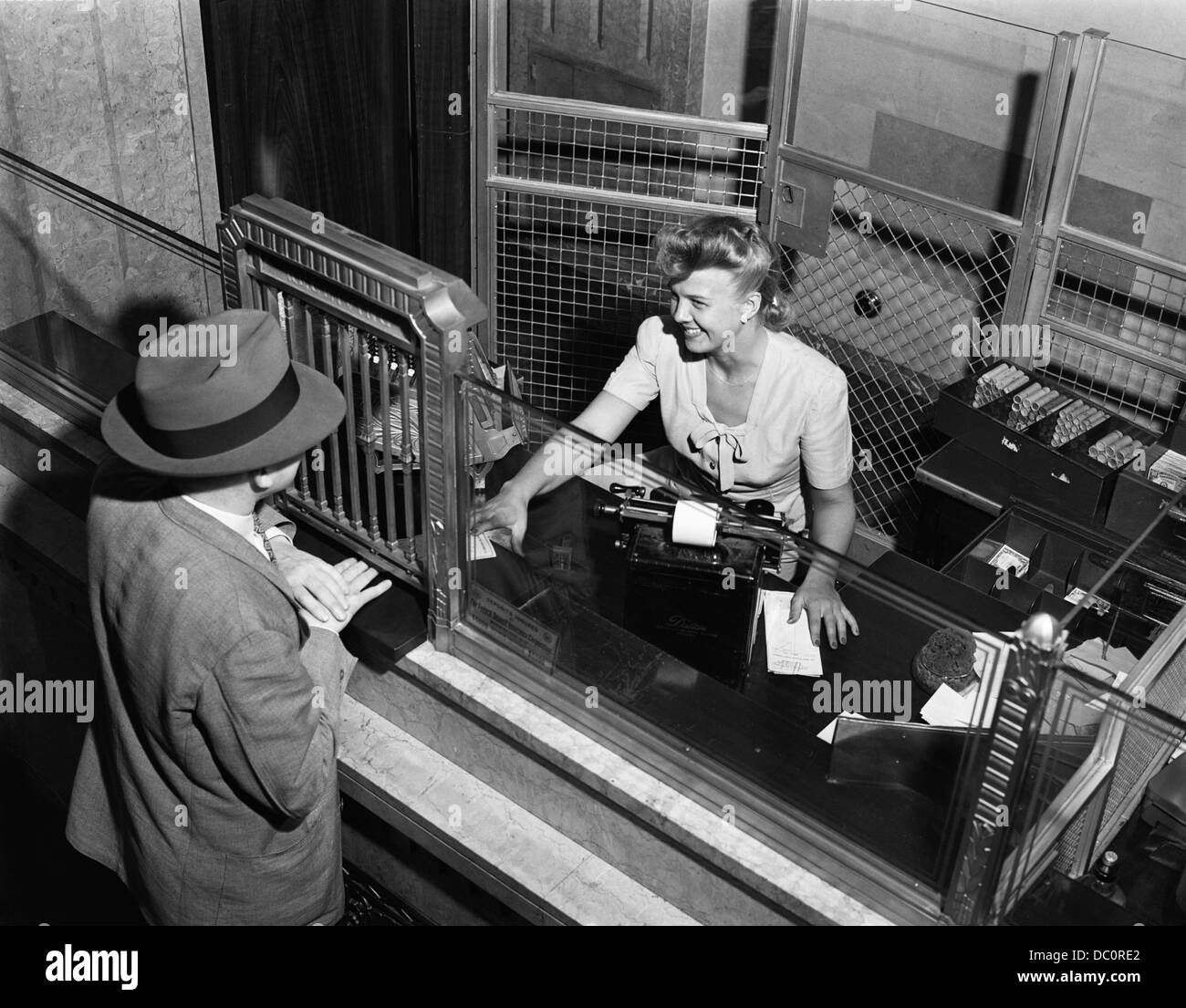 1940s donna BANK TELLER dietro la gabbia di servire clienti maschio Foto Stock