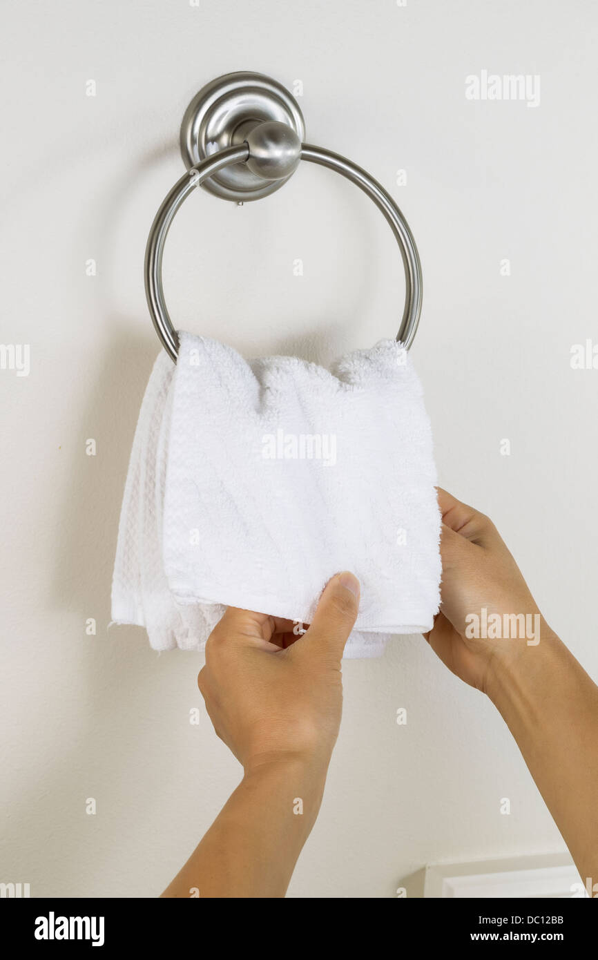 Foto verticale di mani femminili mettendo pulire asciugamano bianco sulla parete anello a gancio nella stanza da bagno Foto Stock