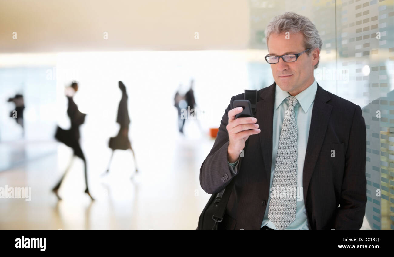 Imprenditore per la messaggistica di testo con un telefono cellulare nella lobby Foto Stock