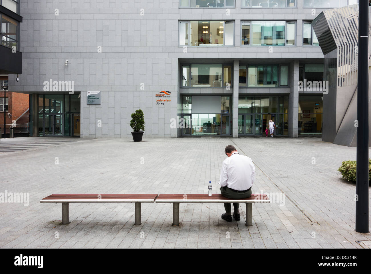 Vista posteriore dell'uomo la lettura mentre è seduto su un banco in piazza / area - Dublino Irlanda Foto Stock