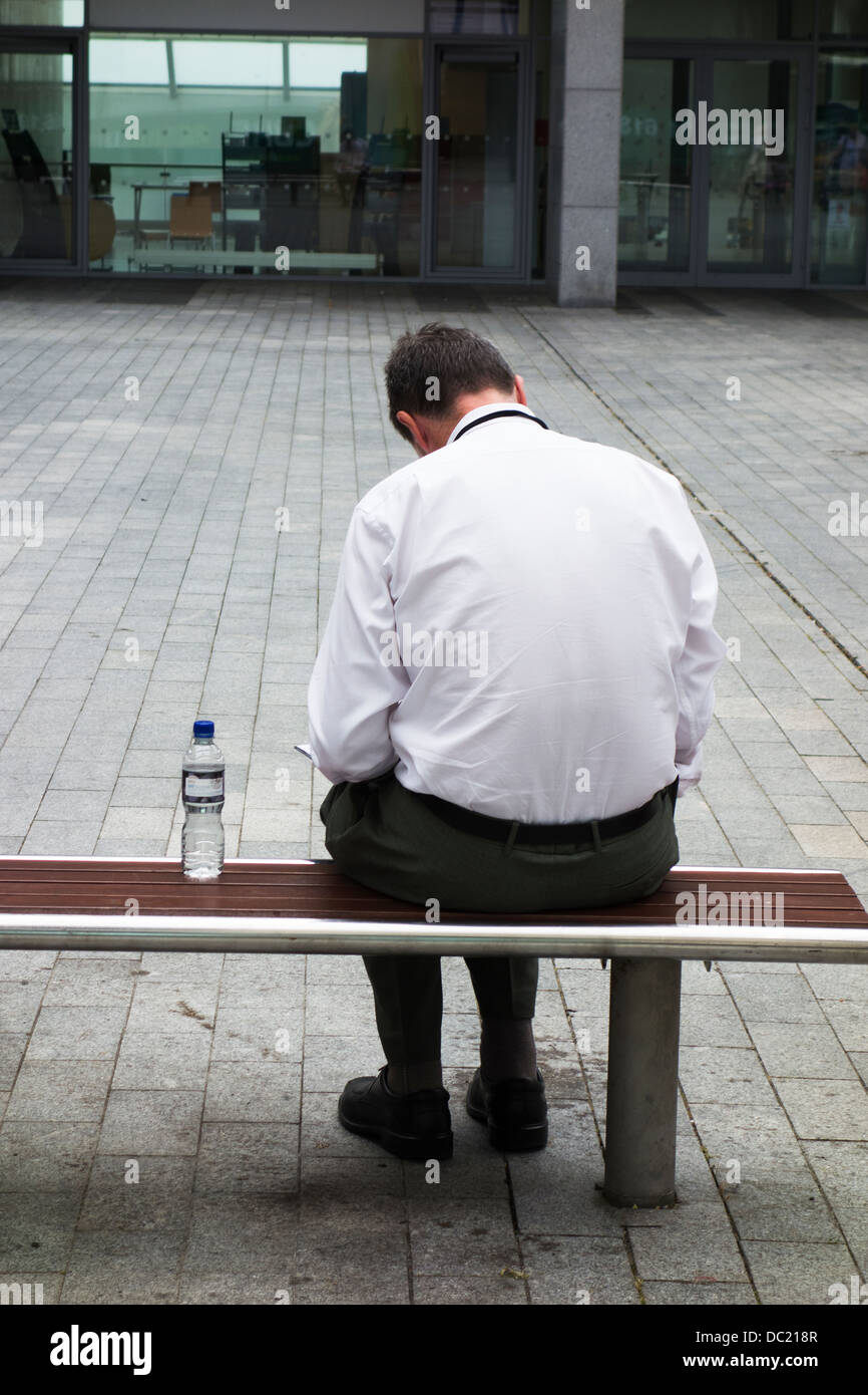 Vista posteriore dell'uomo la lettura mentre è seduto su un banco in piazza / area - Dublino Irlanda Foto Stock