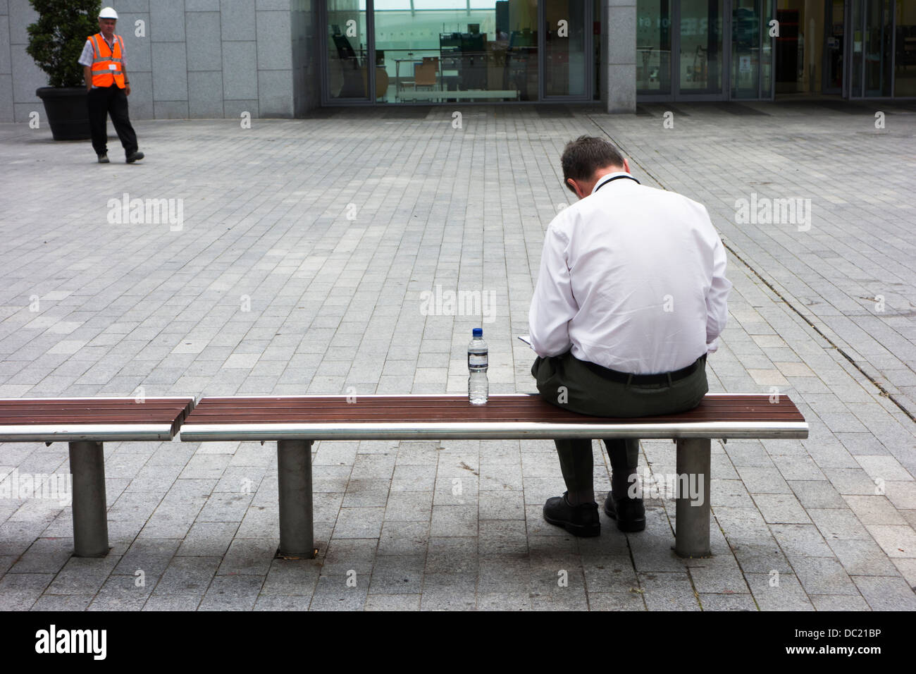 Vista posteriore dell'uomo la lettura mentre è seduto su un banco in piazza / area - Dublino Irlanda Foto Stock