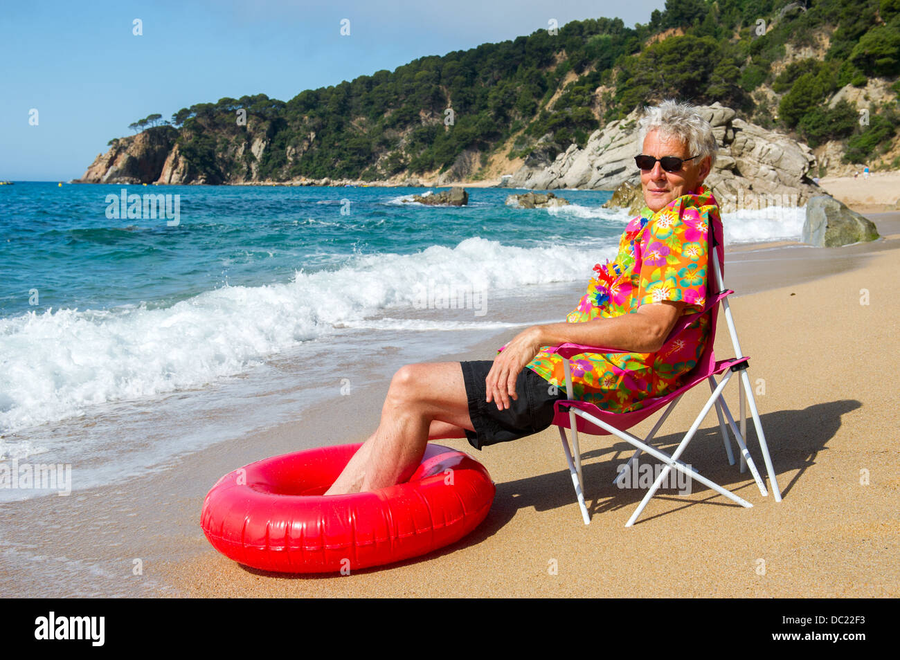 Senior uomo seduto in poltrona con giocattoli al Summer Beach Foto Stock