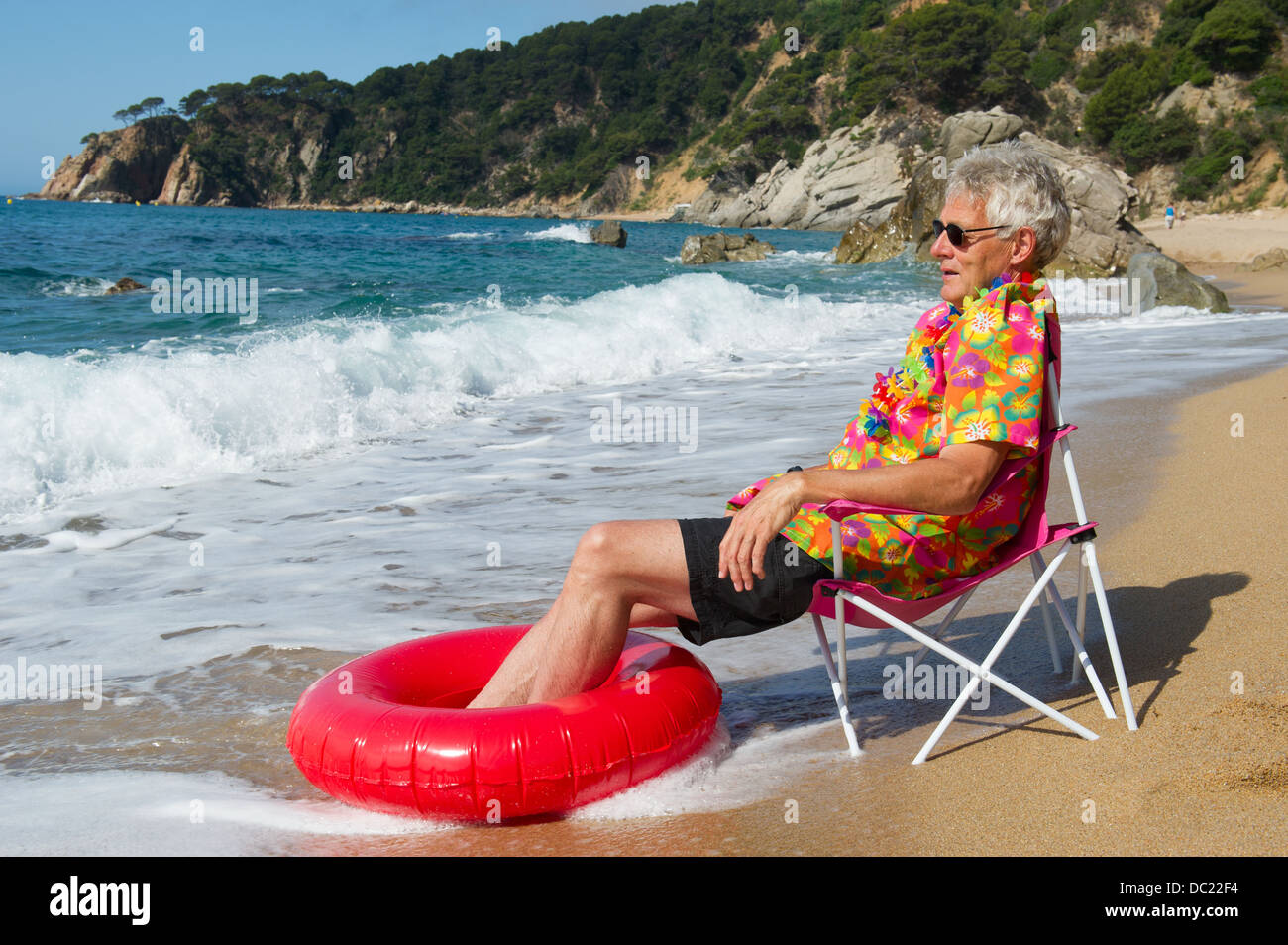Uomo seduto in spiaggia con sedia e hawaii shirt Foto Stock