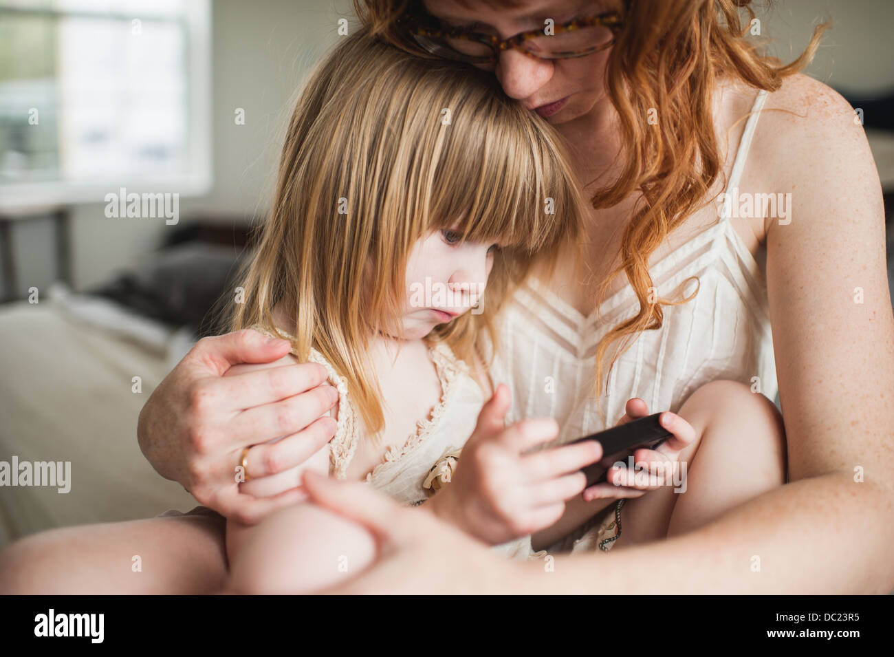 La madre abbraccia la figlia, utilizza lo smartphone Foto Stock