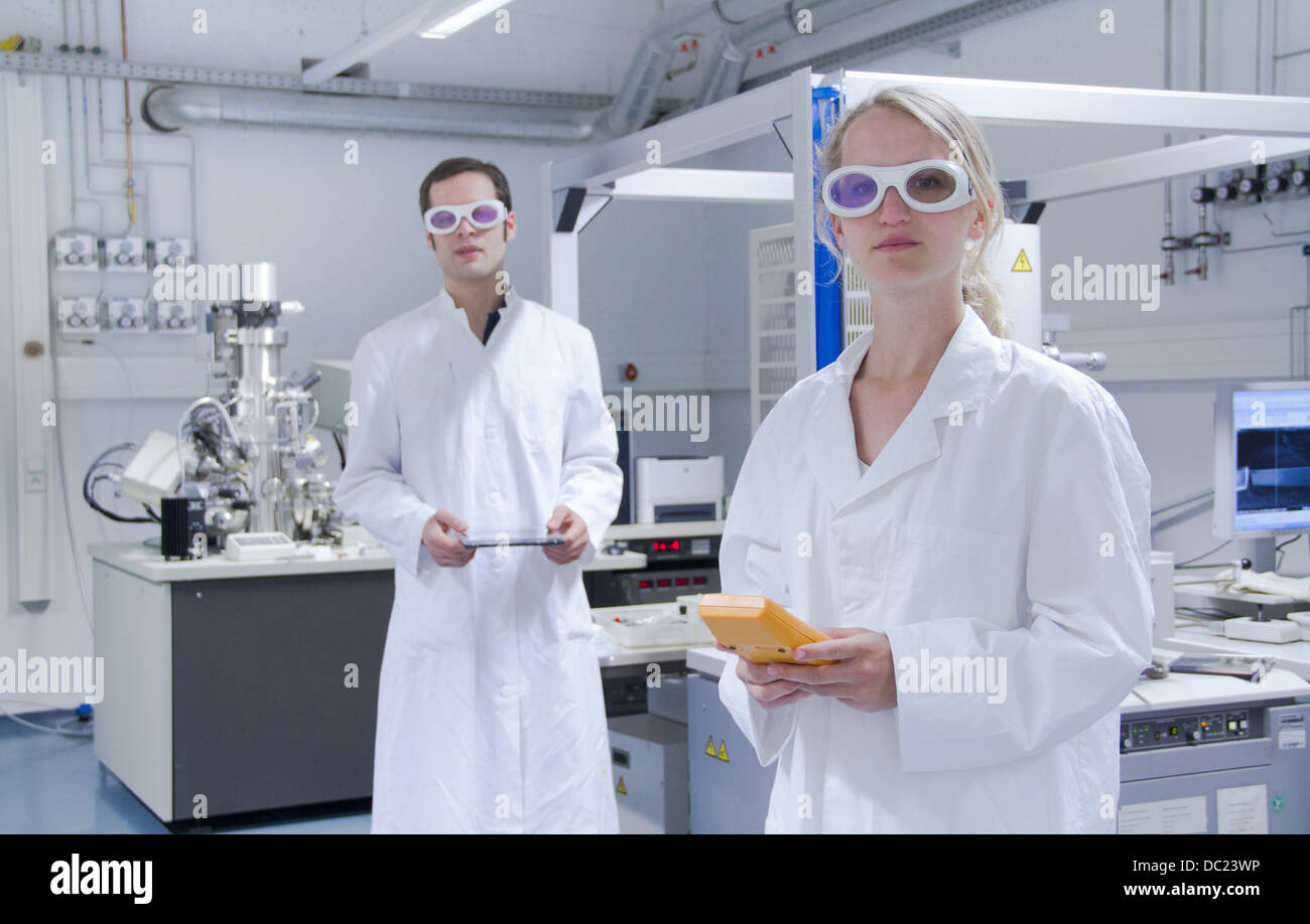 Due scienziati indossando camici da laboratorio e occhiali di sicurezza in piedi in laboratorio Foto Stock