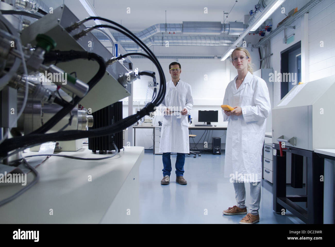 Due scienziati indossando camici da laboratorio e occhiali di sicurezza in piedi in laboratorio Foto Stock