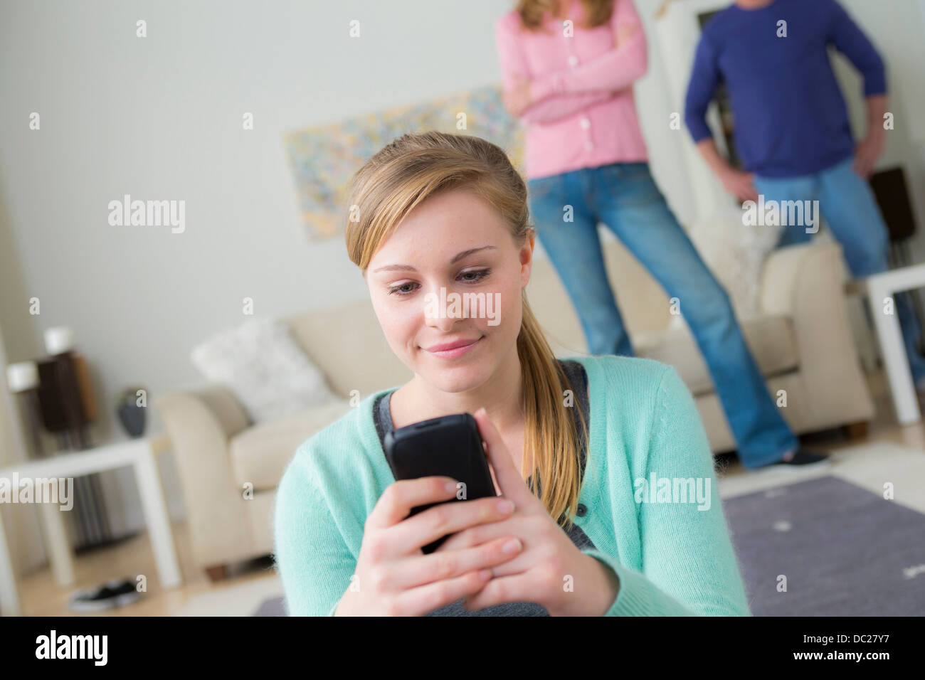 Ragazza adolescente tramite telefono cellulare, i genitori in background Foto Stock