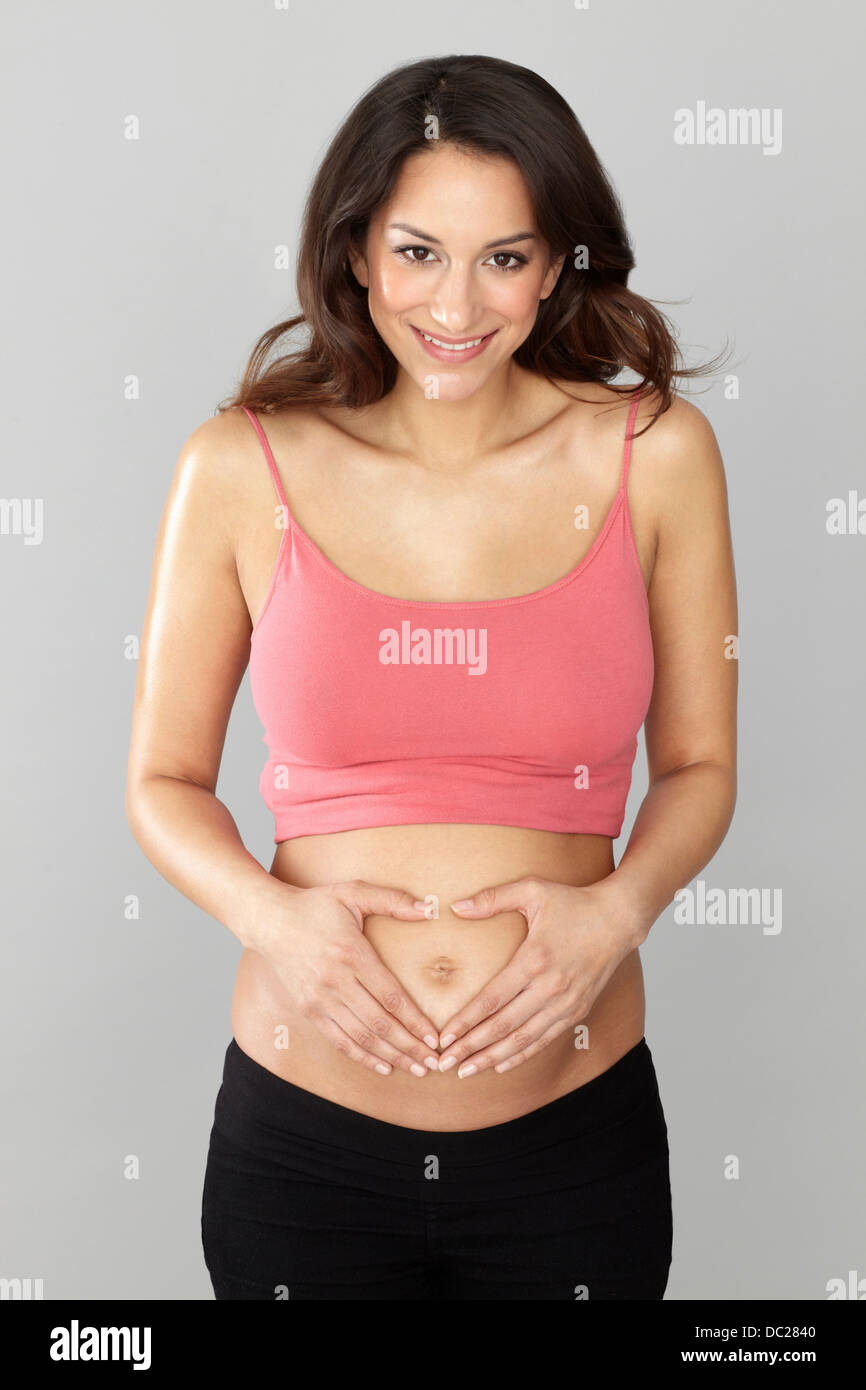 Donna incinta messa a forma di cuore con le mani su stomaco Foto Stock