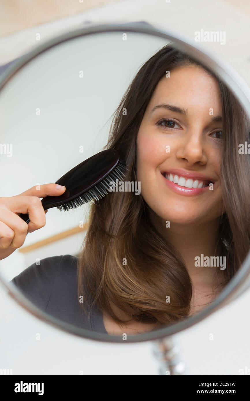 Giovane donna capelli di spazzolatura in specchio Foto Stock