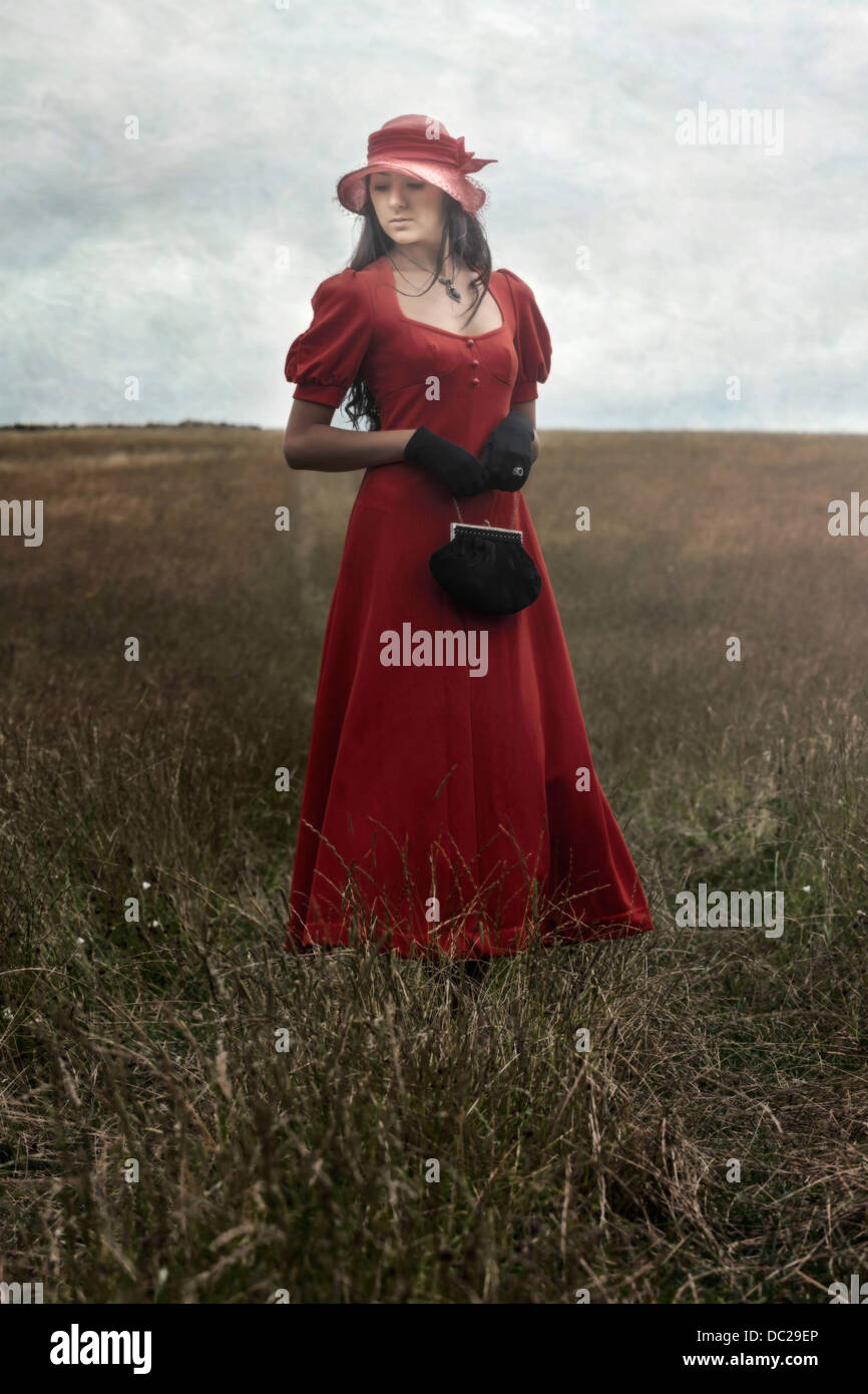 Una ragazza in un abito rosso è in piedi su un campo Foto Stock