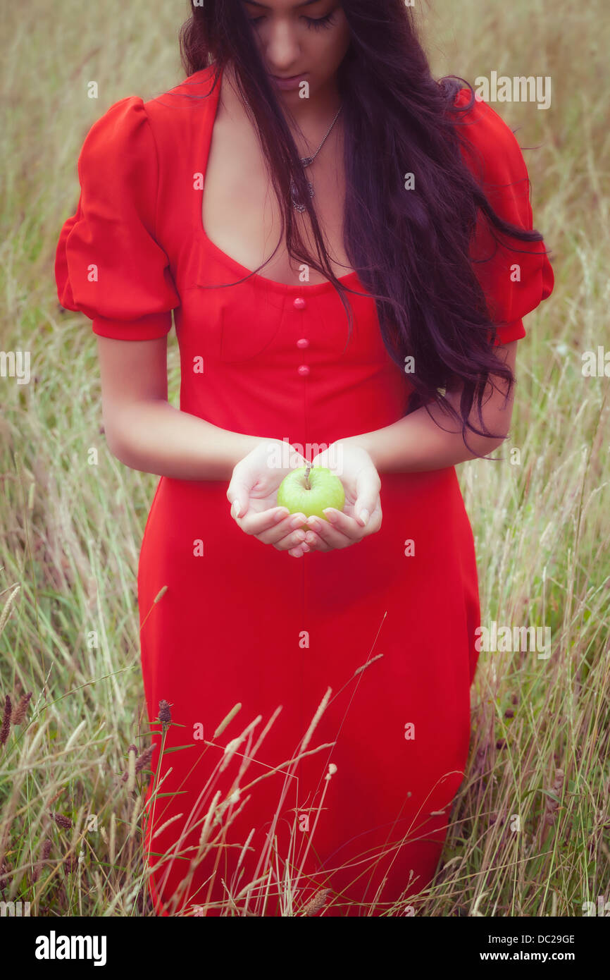 Una ragazza in un abito rosso, tenendo una mela verde Foto Stock