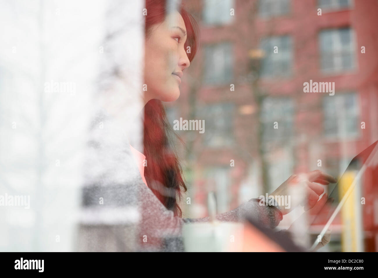 Donna con tavoletta digitale guardando fuori della finestra in vetro Foto Stock