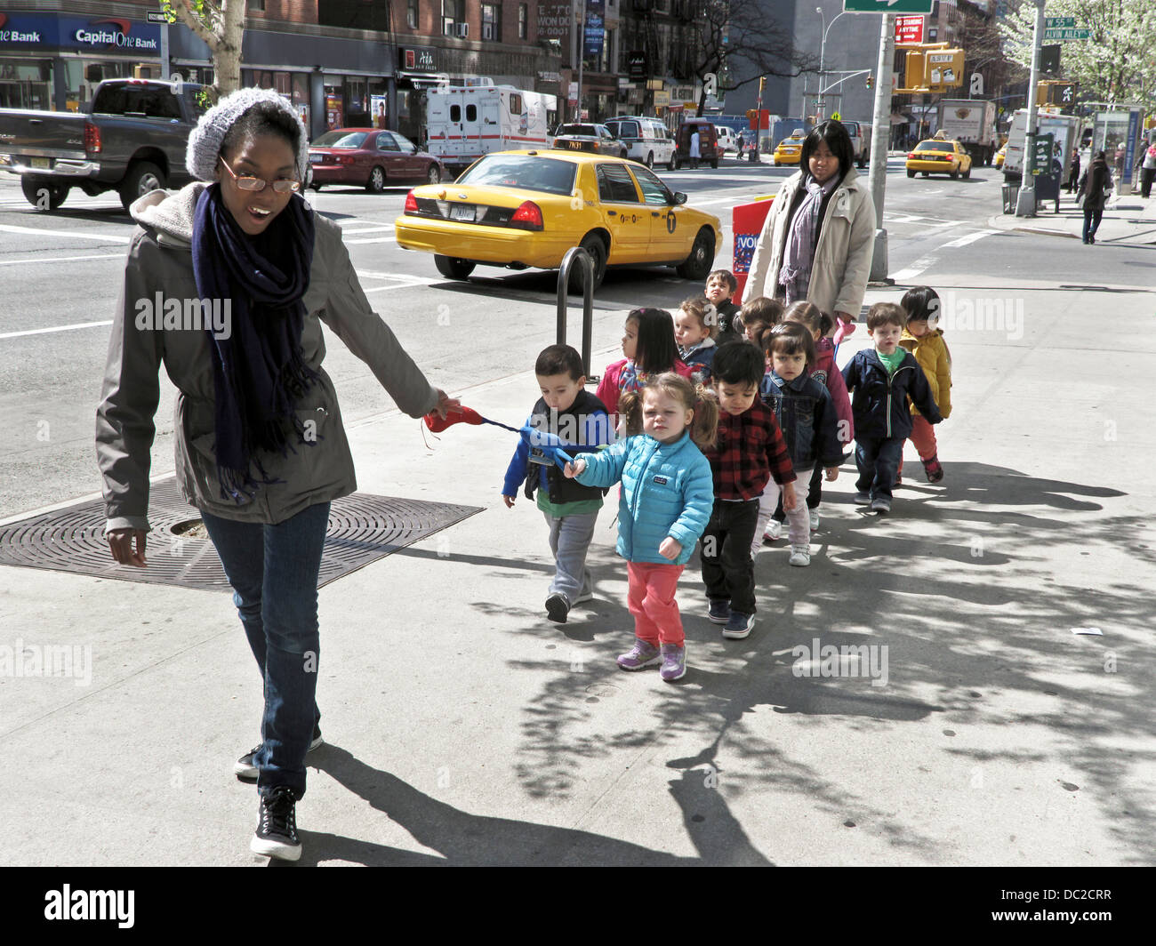 Piccolo gruppo i bambini in età prescolare tethered con nastro colorato di essere prese in considerazione per una passeggiata da 2 adulto nero donne sulla gelida giornata di primavera New York Foto Stock