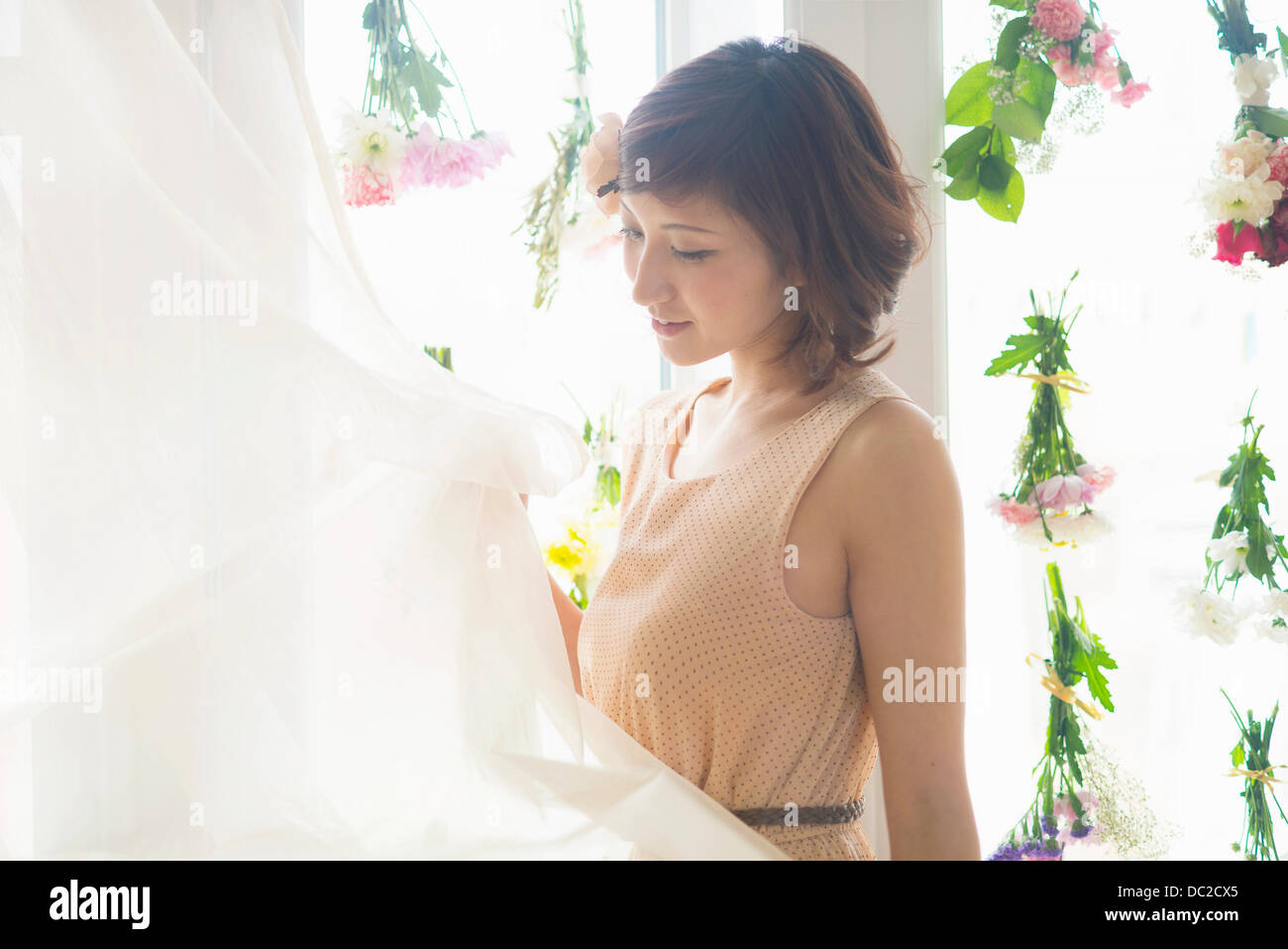 La donna tende di sollevamento delle finestre di vetro con fiori penzolanti Foto Stock