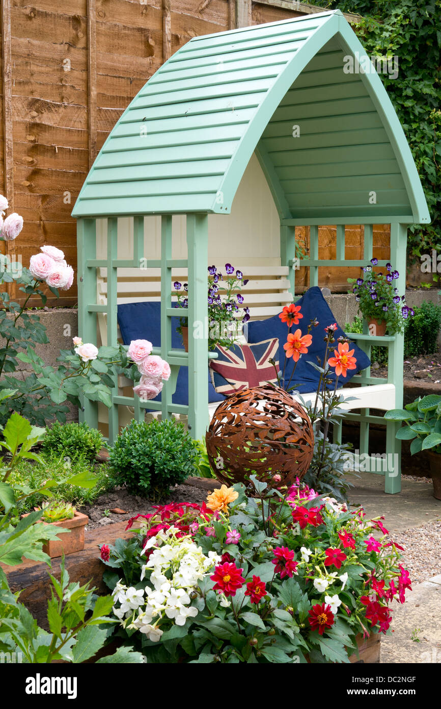 Verde pergolato in legno posti a sedere nel giardino Inglese con fiori dahlia e rusty sfera di legno, Inghilterra Foto Stock