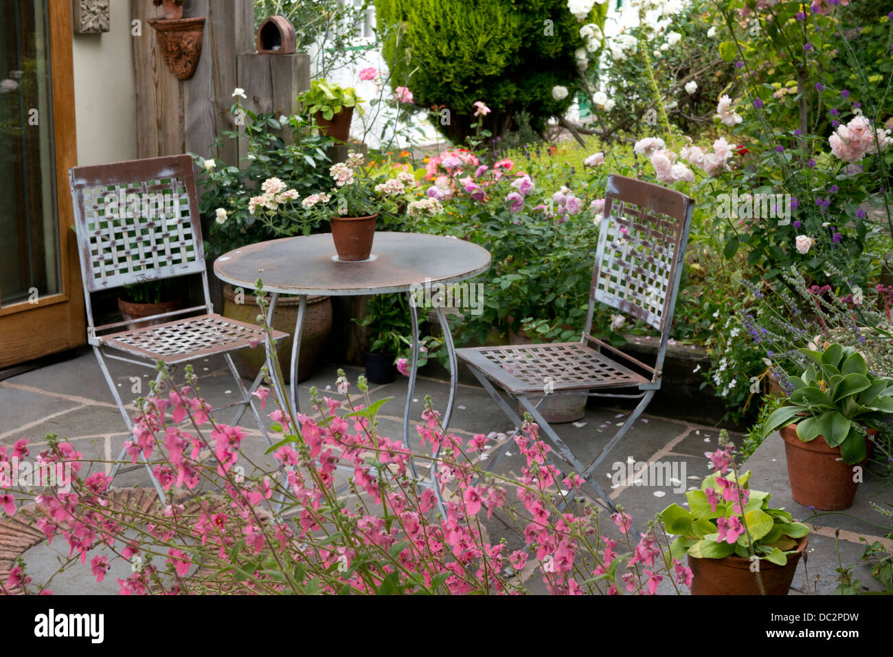 Inglese estate patio in pietra con metallo mobili da giardino orlato da rosa rose e fiori Diasica, Inghilterra Foto Stock