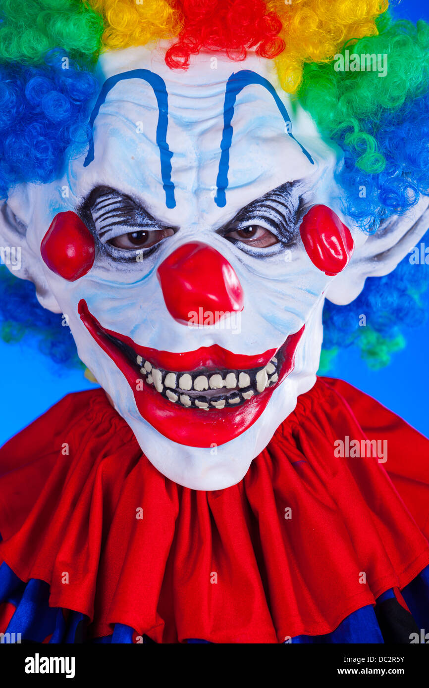 Scary clown persona nella maschera di clown su sfondo blu studio shot Foto Stock