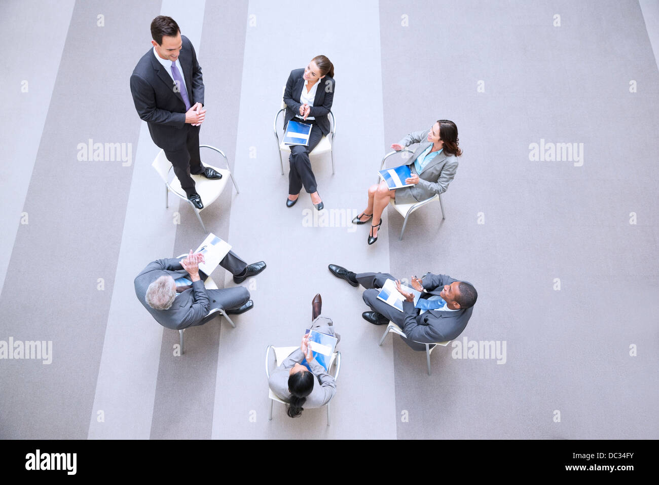 Elevato angolo di visione di imprenditore in piedi su una sedia in cerchio con co-lavoratori Foto Stock