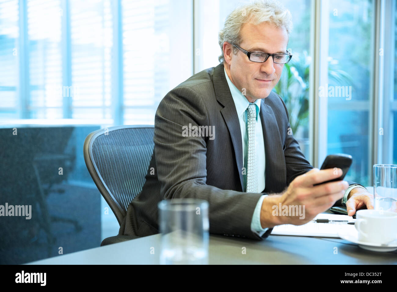 Imprenditore per la messaggistica di testo con il cellulare in sala conferenze Foto Stock