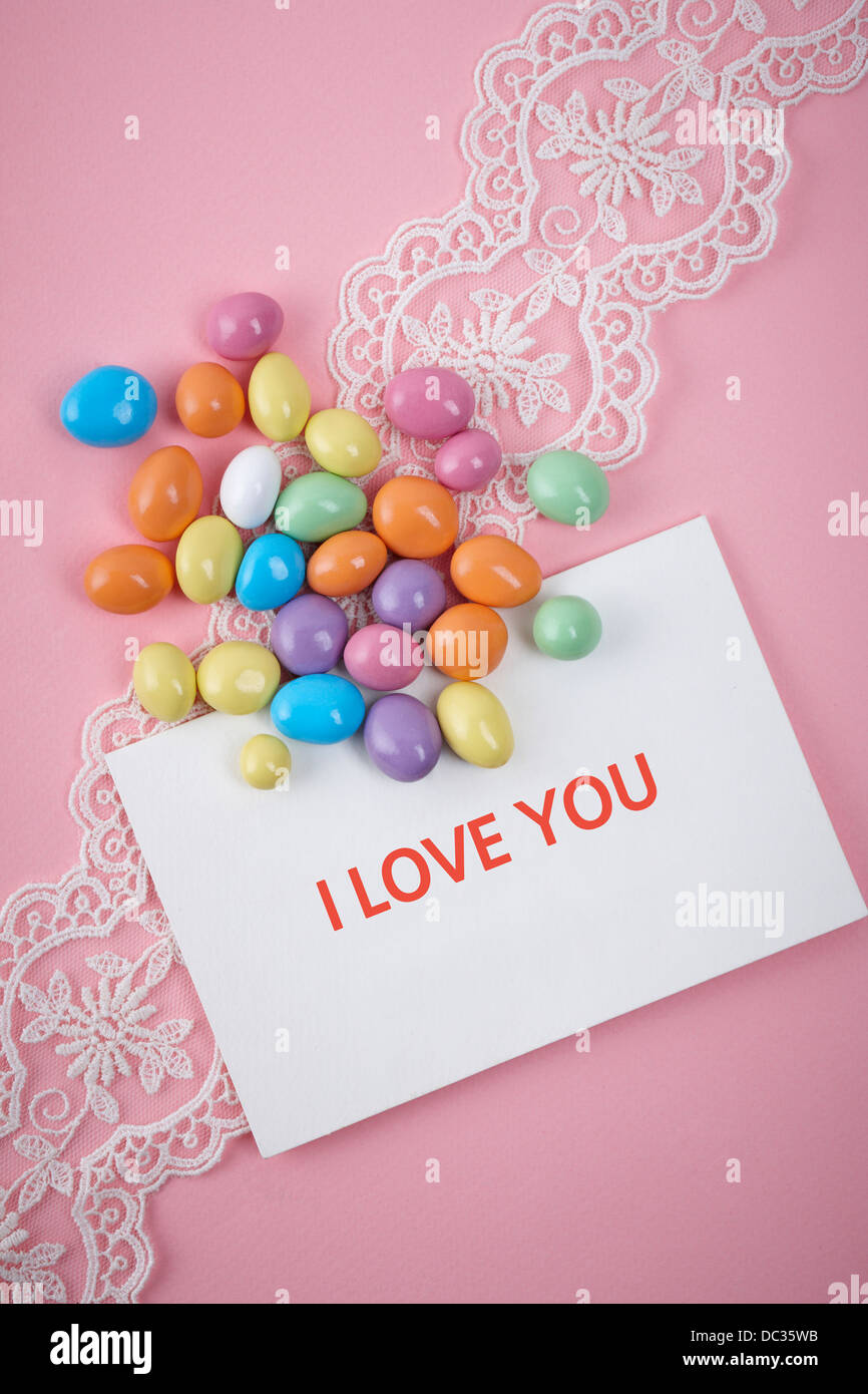 Caramelle colorate su sfondo rosa con una lettera ti amo Foto Stock