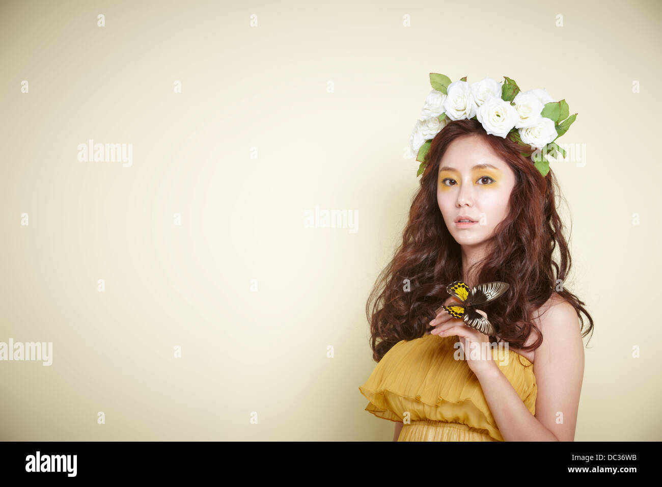 Una signora in abito con ghirlanda di fiori sulla testa in posa con farfalla Foto Stock