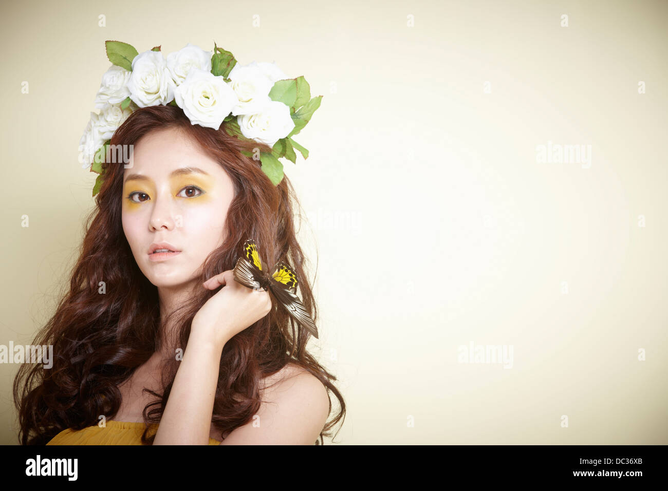 Una signora in abito con ghirlanda di fiori sulla testa in posa con farfalla Foto Stock
