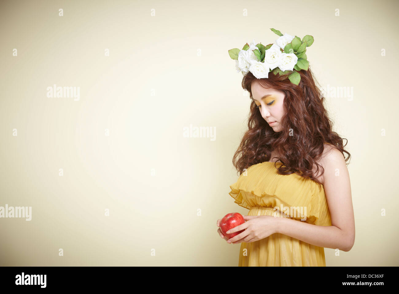 Una signora in abito con ghirlanda di fiori sulla testa tenendo un Apple Foto Stock