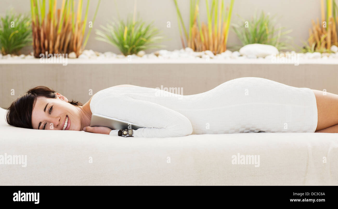 Ritratto di donna sorridente azienda digitale compressa e posa sul patio divano Foto Stock