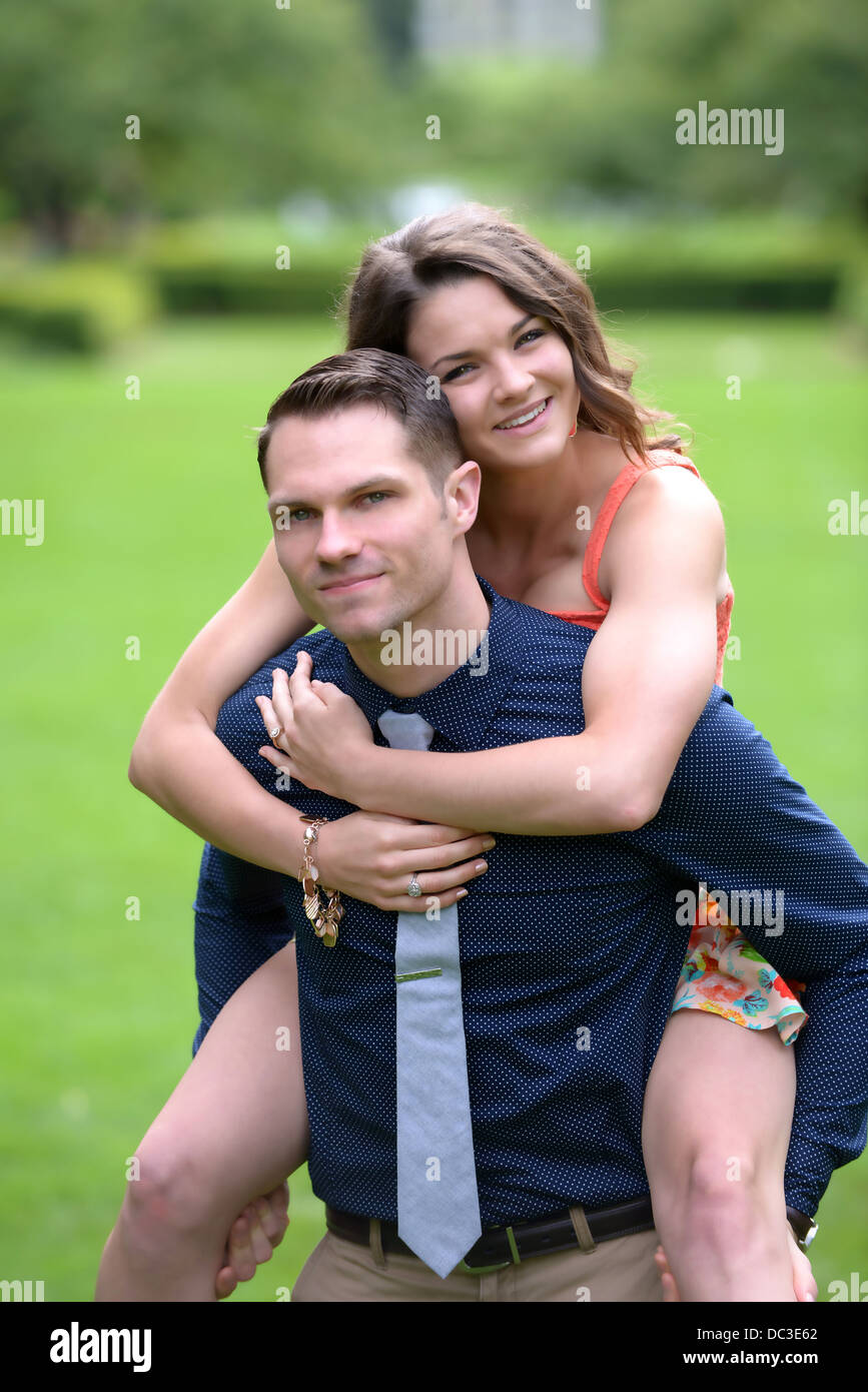 Un attraente coppia giovane in un giardino con l'uomo che porta la sua fidanzata sulla schiena. Foto Stock