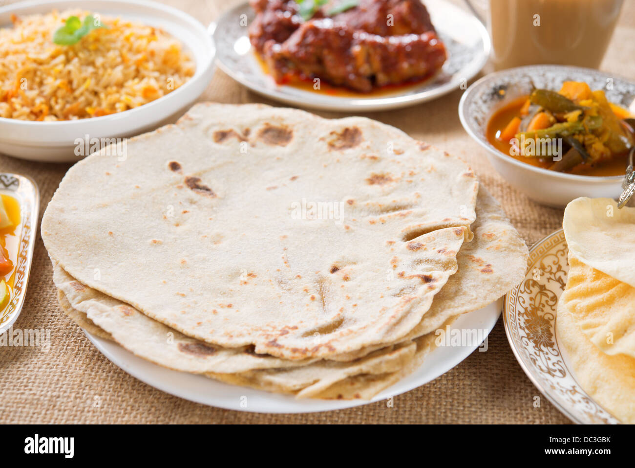 Chapatti roti, pollo e curry, biryani riso, insalata, masala latte e tè papadom. Il cibo indiano sul tavolo da pranzo. Foto Stock