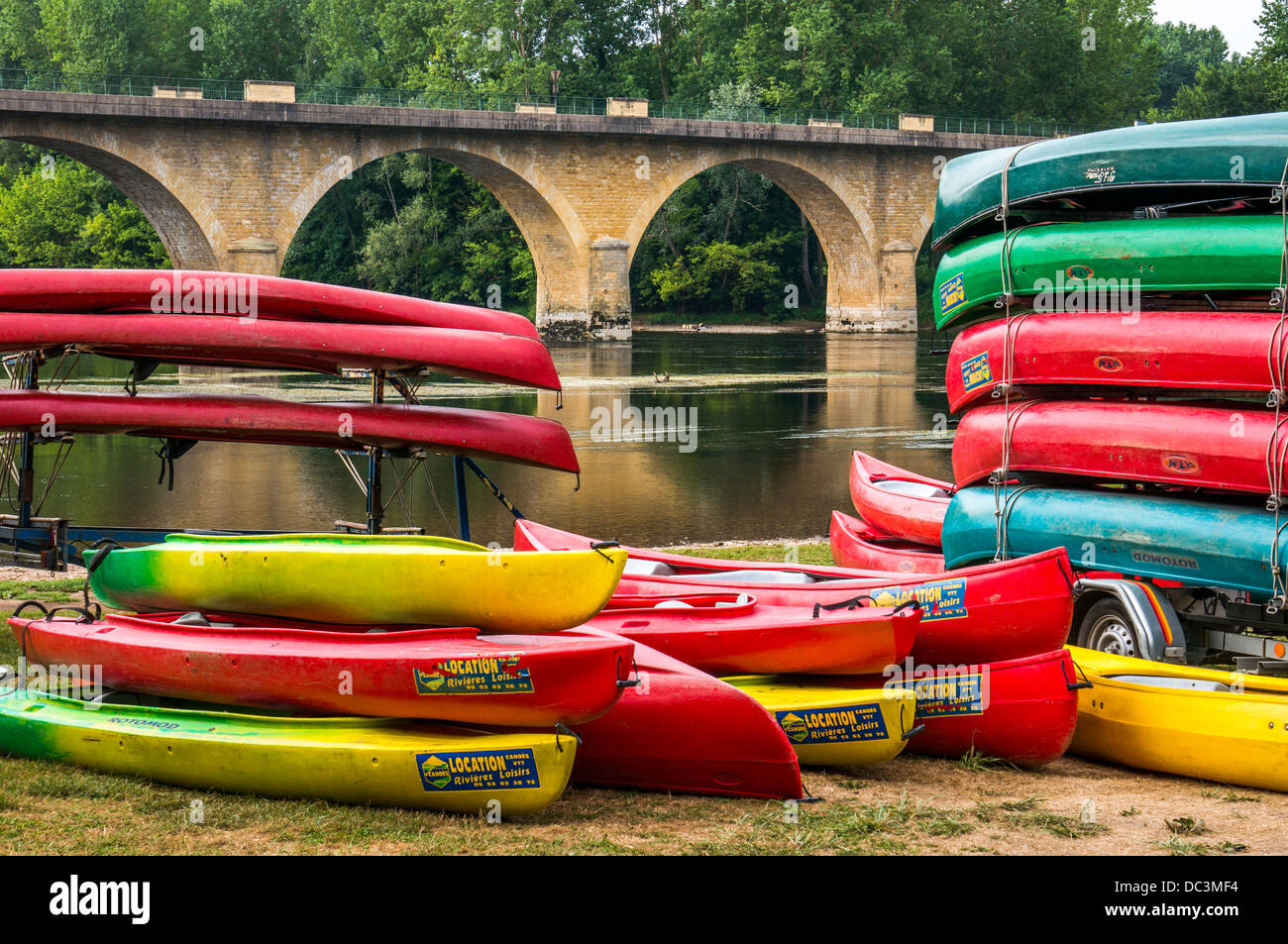 Canoe colorati impilati per il noleggio in prossimità di un ponte sul fiume a Limeuil, dove la Dordogne e Vézère fiumi si incontrano, a sud ovest della Francia. Foto Stock