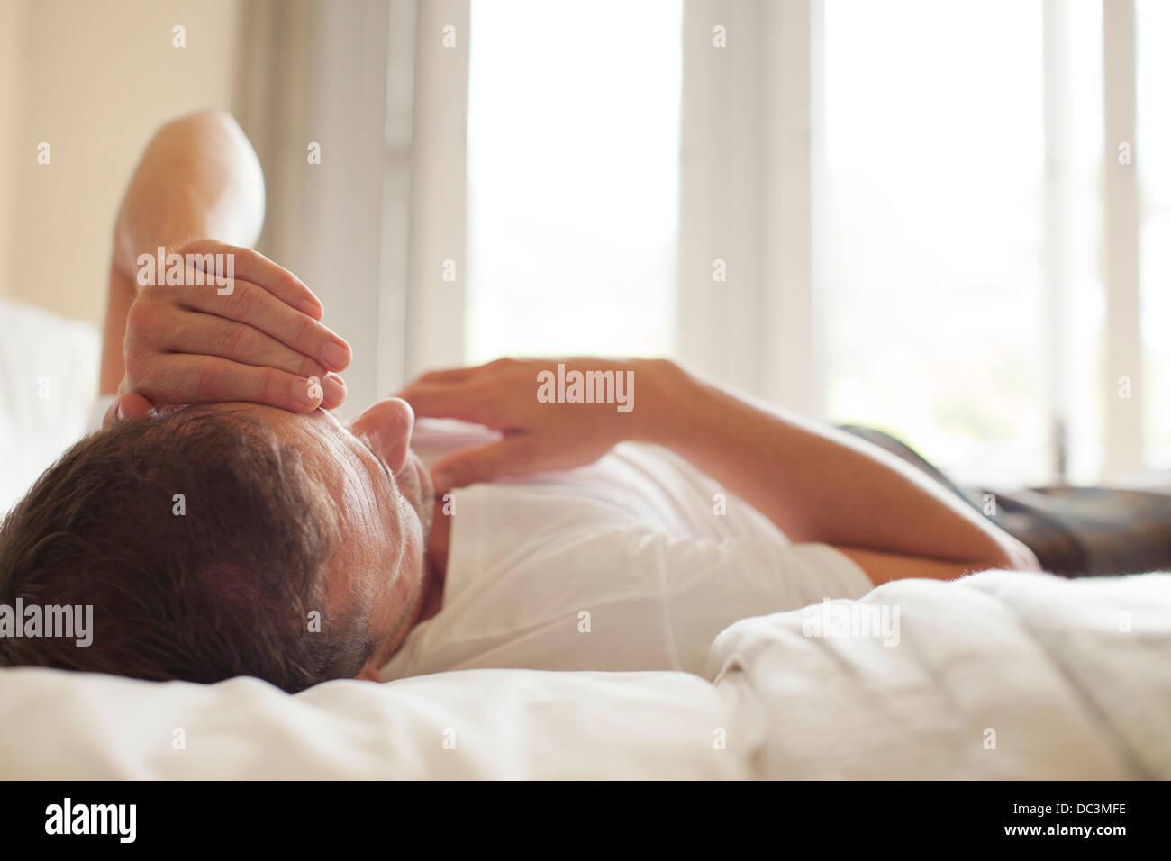 Uomo che stabilisce nel letto con testa in mani Foto Stock