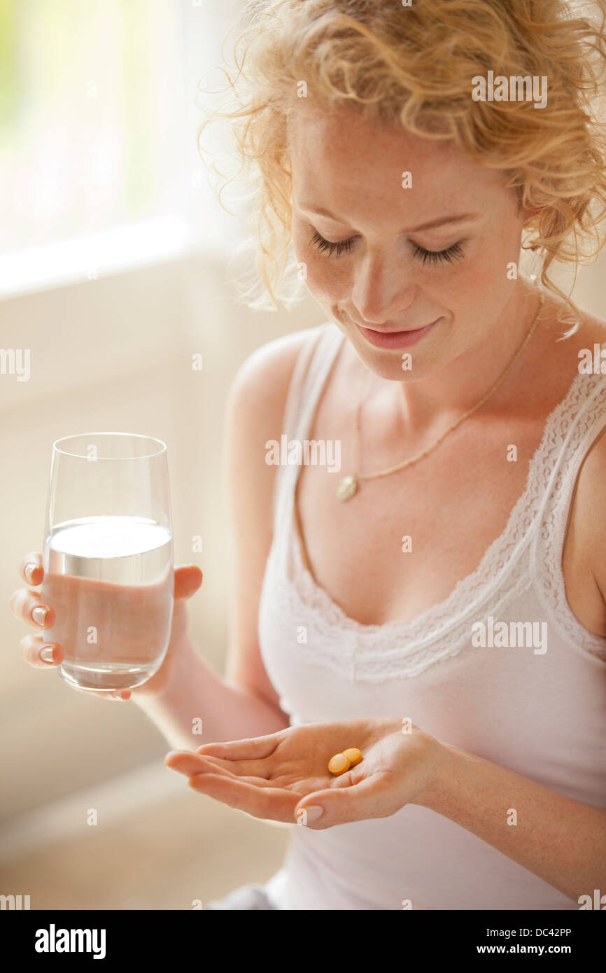 Donna che mantiene un bicchiere di acqua e pillole Foto Stock