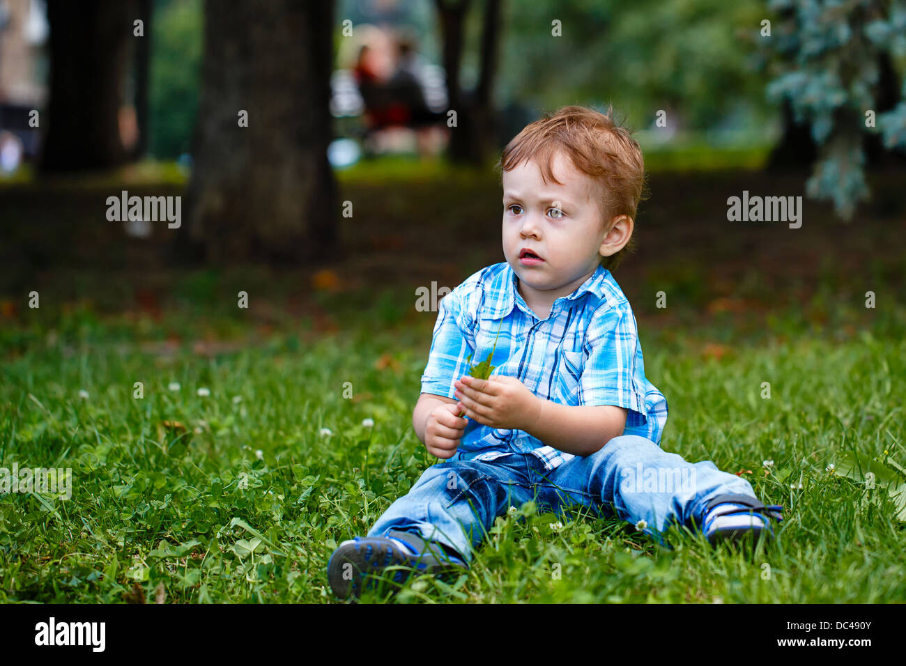 Little Boy in jeans e un plaid shirt seduto sull'erba nel parco Foto Stock