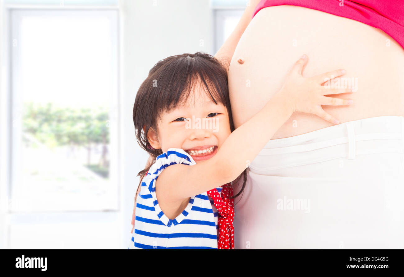 Felice bambina abbracciando la gravidanza di una madre di ventre Foto Stock