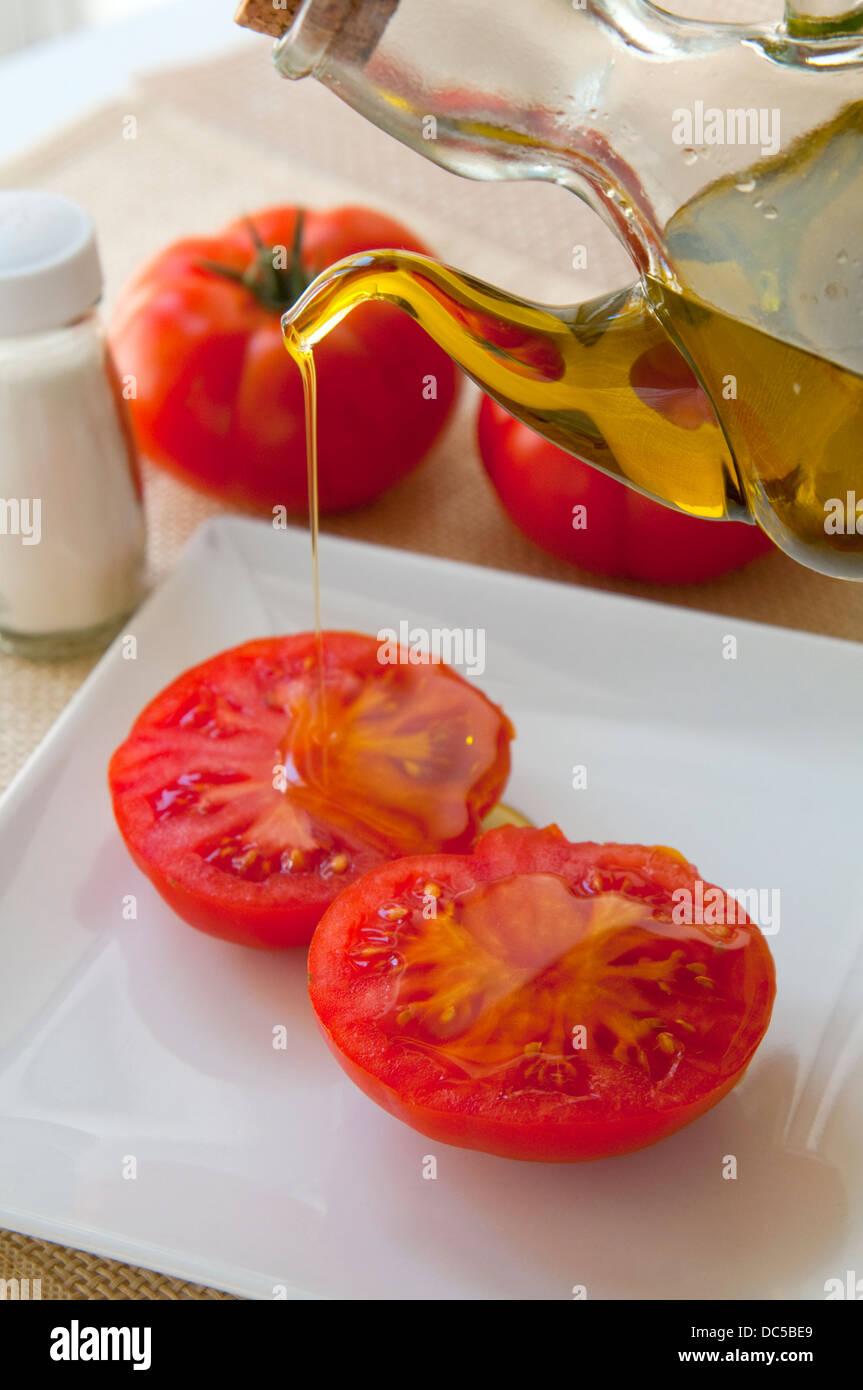 Bottiglia di Olio versando olio di oliva su un pomodoro a fette. Foto Stock