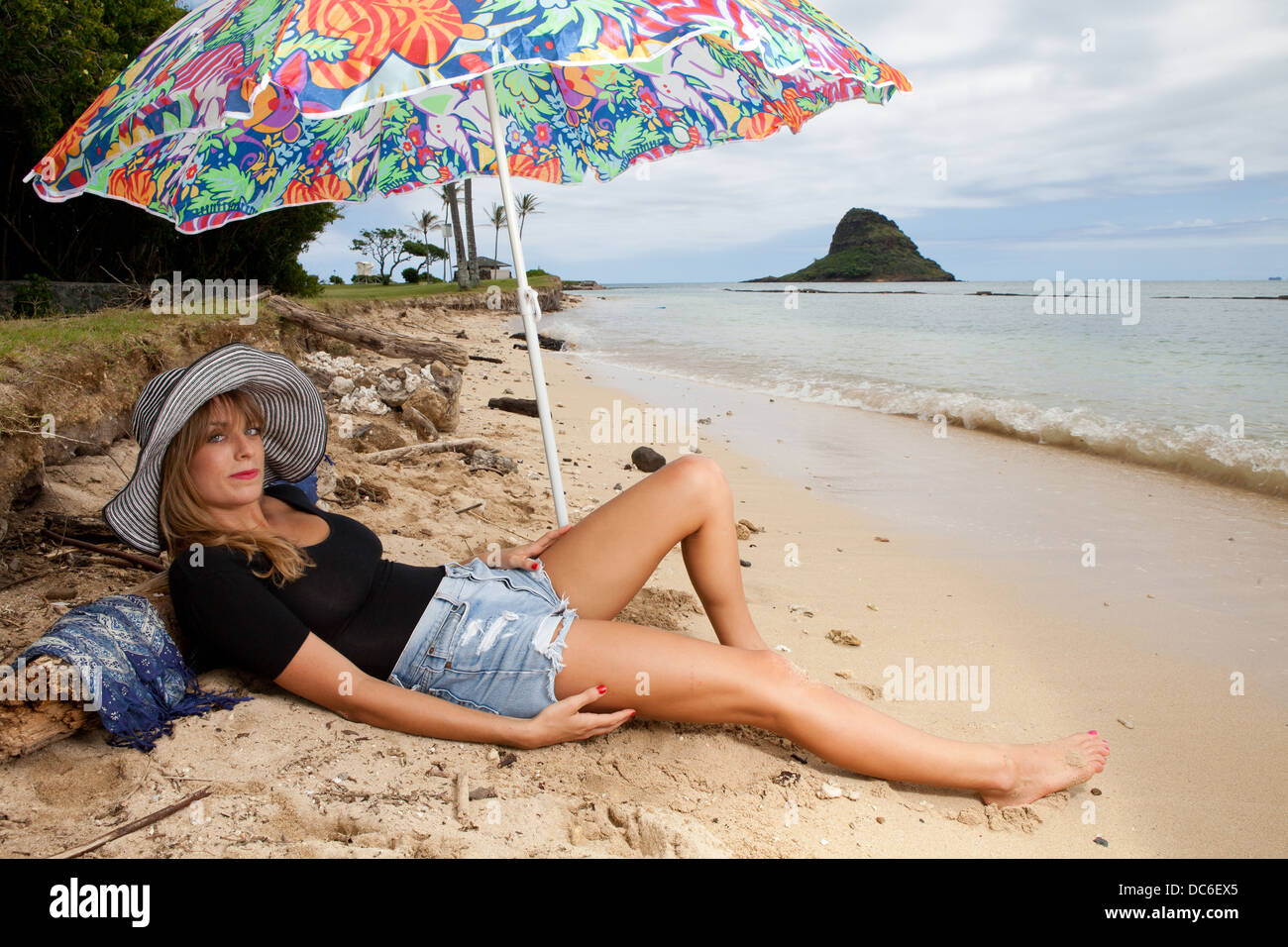 Una bionda donna caucasica giace sotto il suo ombrello su una spiaggia alle Hawaii. Foto Stock