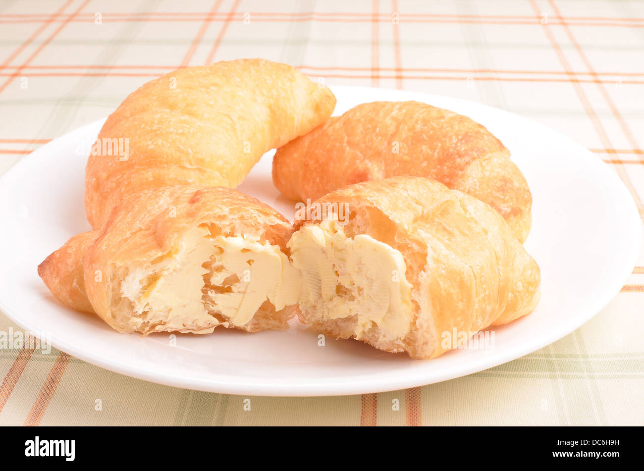 Tre i croissant sono su un piattino bianco con un croissant lacerata con burro spalmato su di esso. Foto Stock