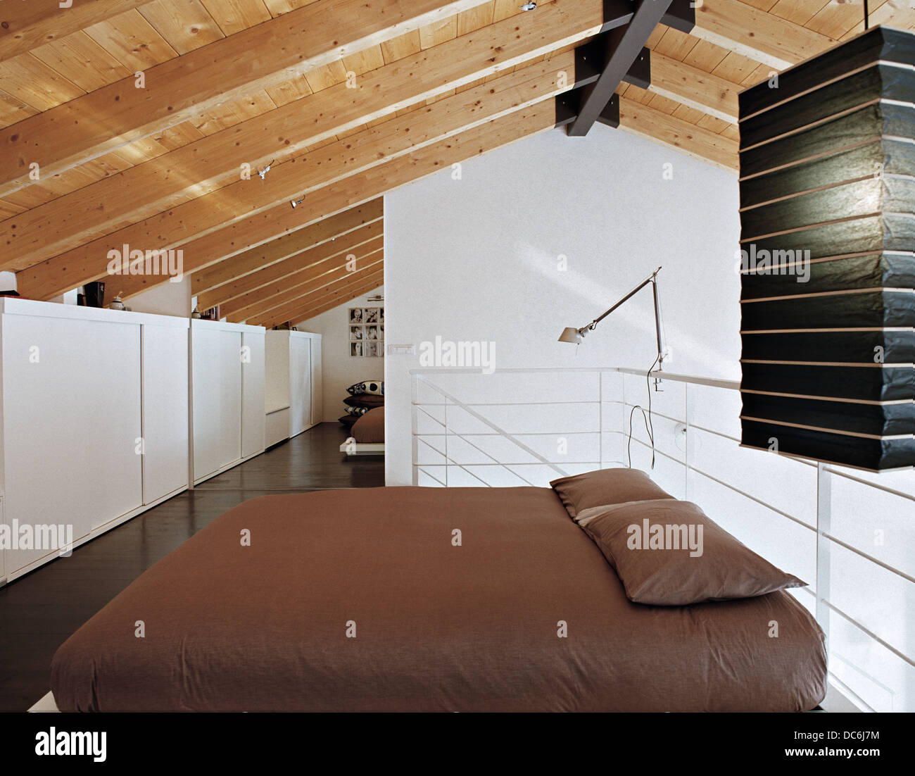 Letto matrimoniale sul soppalco in una moderna camera da letto con soffitto in legno e pavimento in legno Foto Stock