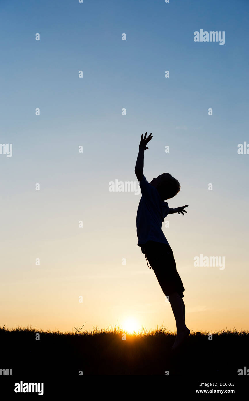 Ragazzo salta con le braccia in aria al tramonto. Silhouette Foto Stock