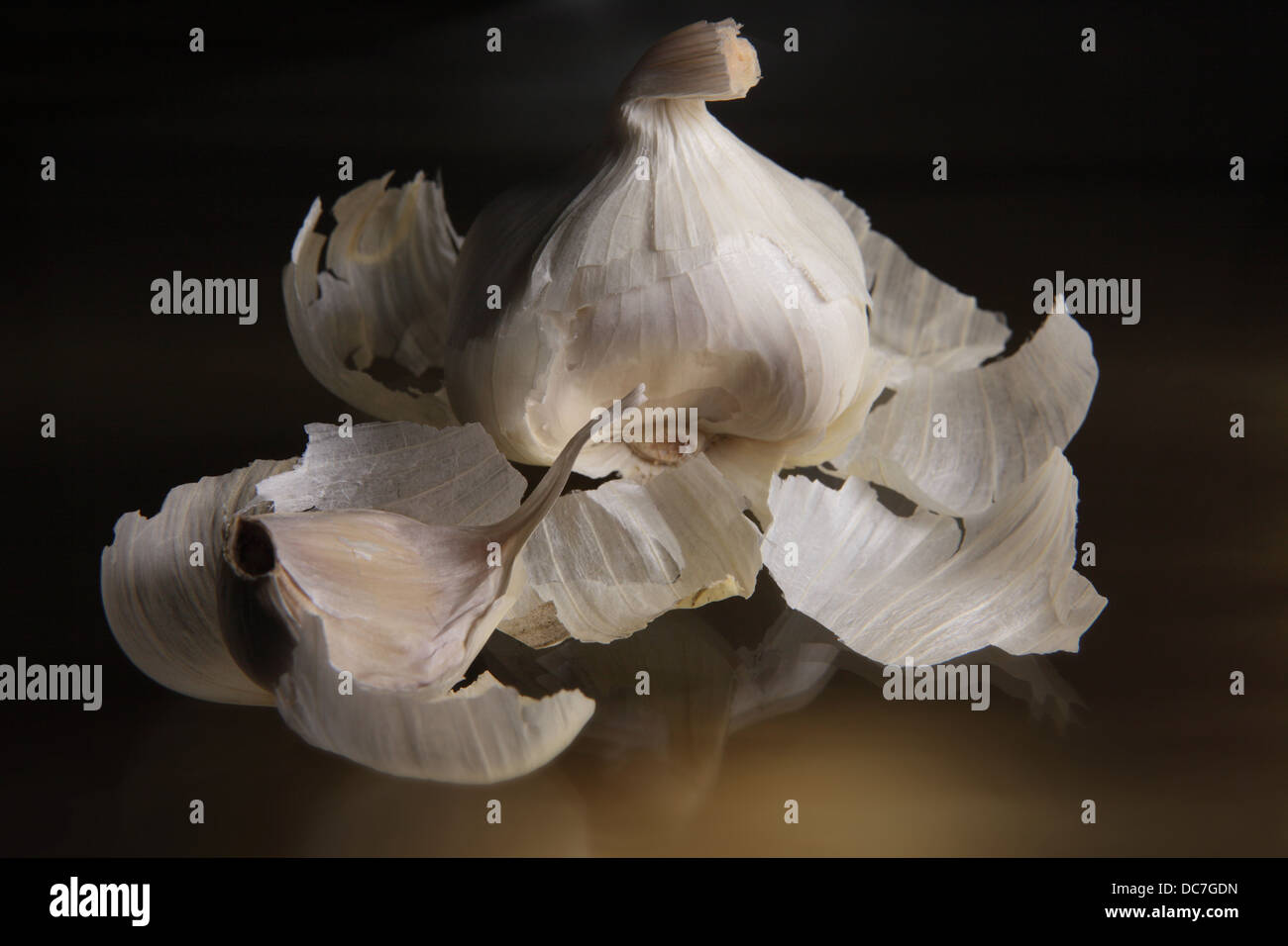 Spicchio di aglio in primo piano e una testa di aglio in background.La superficie su cui sono posizionati è scuro e il riflettente Foto Stock