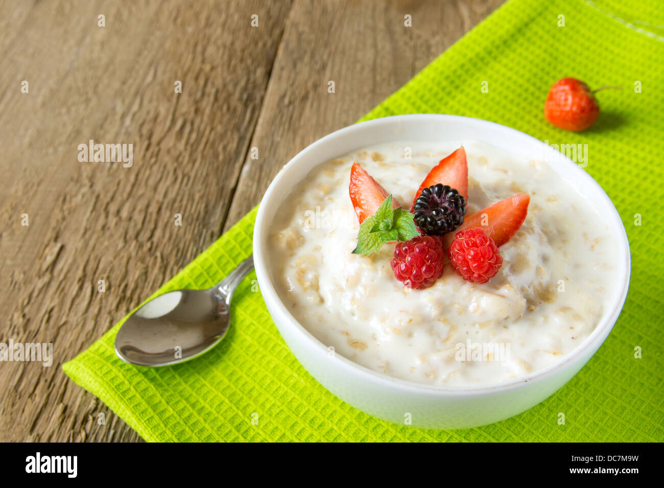 Caldo fresco fiocchi d'avena porridge con le bacche e le foglie di menta sul tovagliolo e tavolo in legno, close up, orizzontale, copia dello spazio. Vegetaria sani Foto Stock