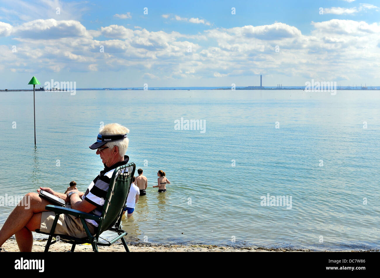 Uomo anziano seduto sul lungomare la lettura di libri elettronici Foto Stock