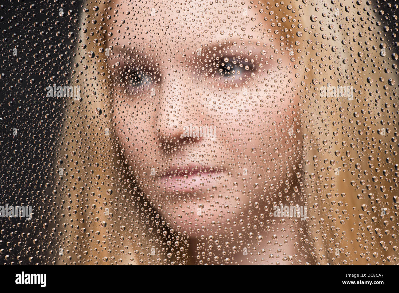 Ritratto di giovane donna bionda adolescente guardando fuori della finestra coperto con gocce di pioggia Foto Stock